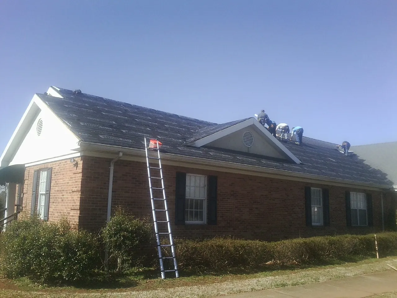 Crew tearing shingles off a brick ranch roof with a ladder set — Metal Roof Repair work by our crew in Sperryville