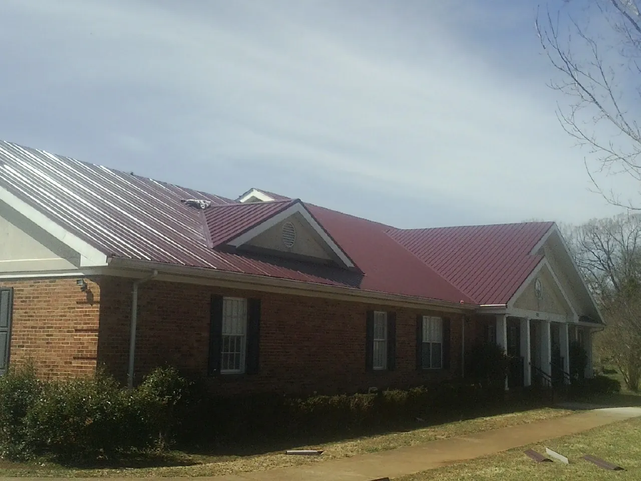 Red metal roof with gabled entries on a long brick building, from a Hail Damage Roof Repair job in Sperryville