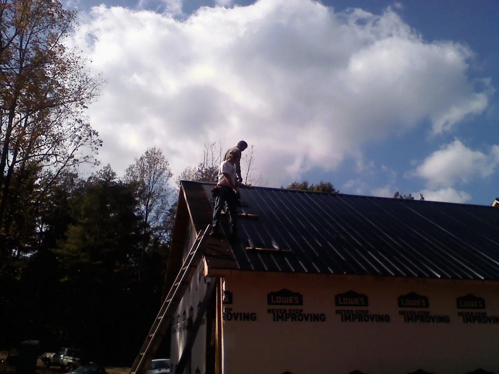 Roofer fastening dark metal panels high against a cloudy sky, from a Roof Inspection job in Sperryville