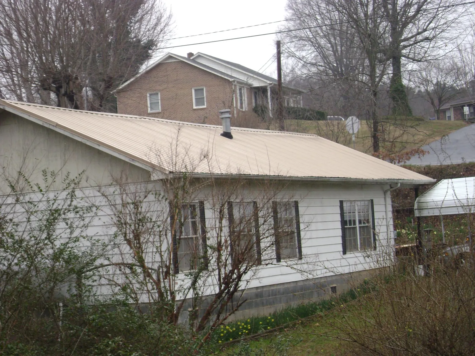 Tan metal roof on a white sided house set into a hillside — Commercial Roofing by Roofing Brothers in Sperryville